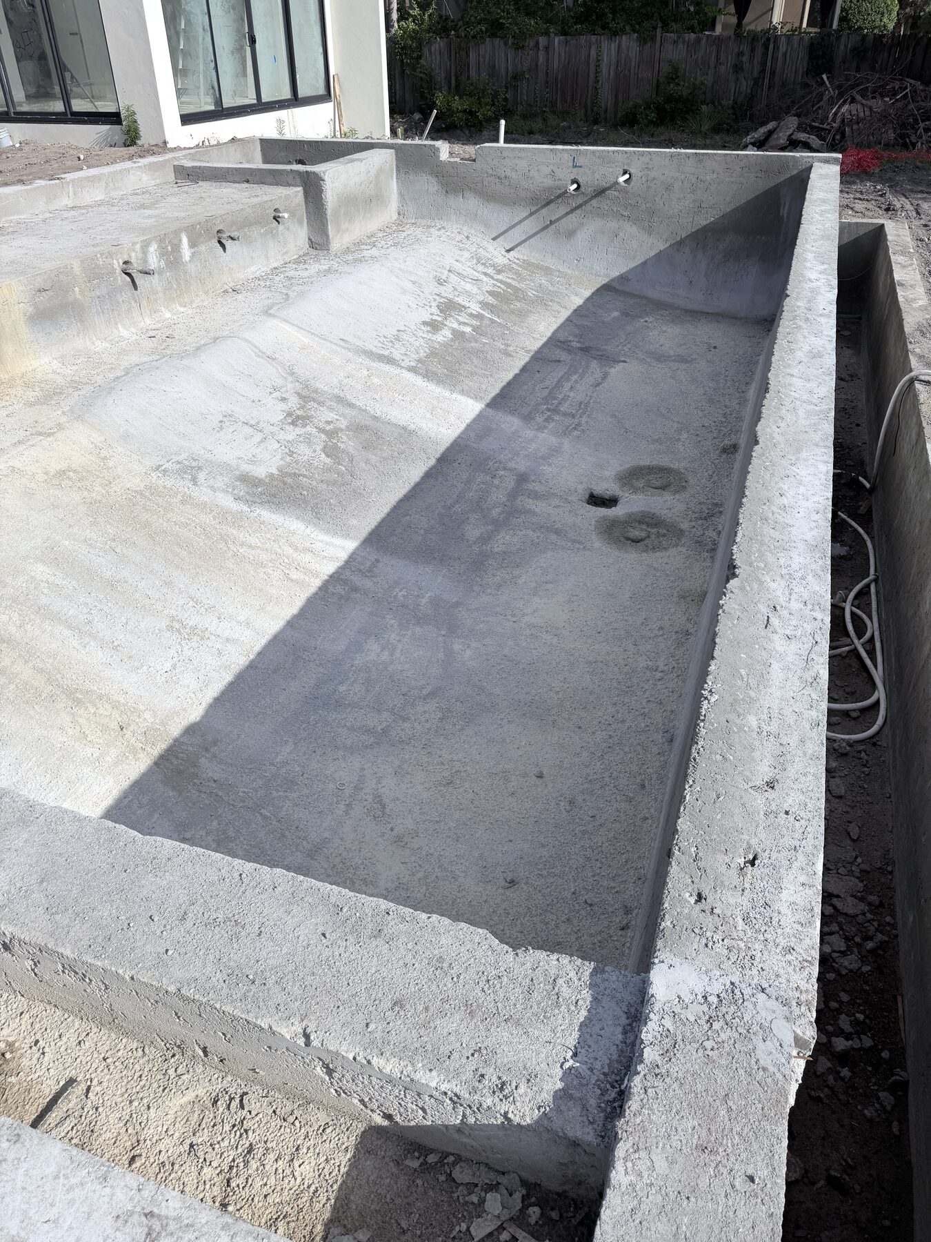 Overall view of the unfinished concrete pool shell with plumbing penetrations