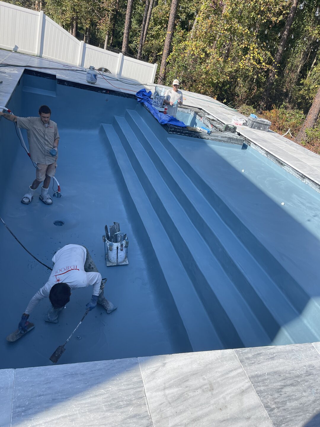 Pool technicians working on the pool interior and steps during midday construction progress.