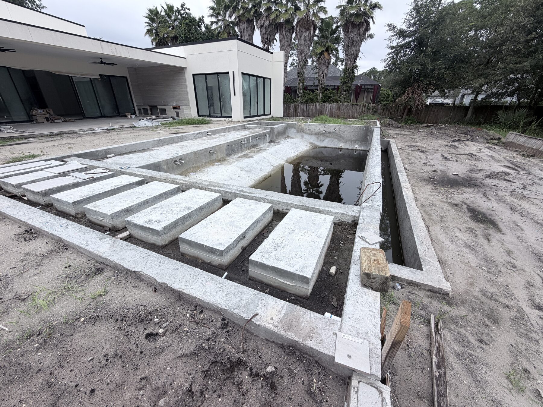 Close view of the unfinished pool shell and broad concrete steps beside the home